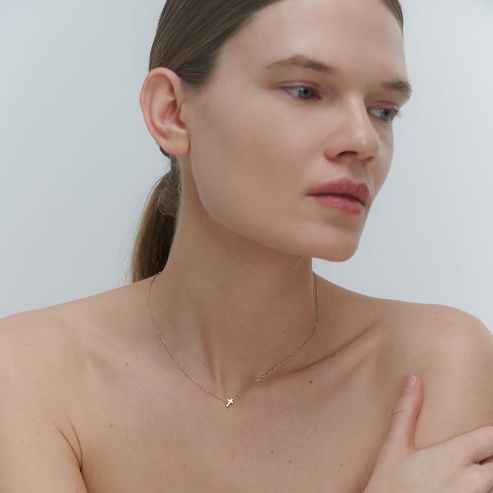 Woman wearing a delicate gold necklace with cross pendant against a plain background