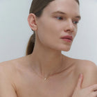 Woman wearing a delicate gold necklace with cross pendant against a plain background