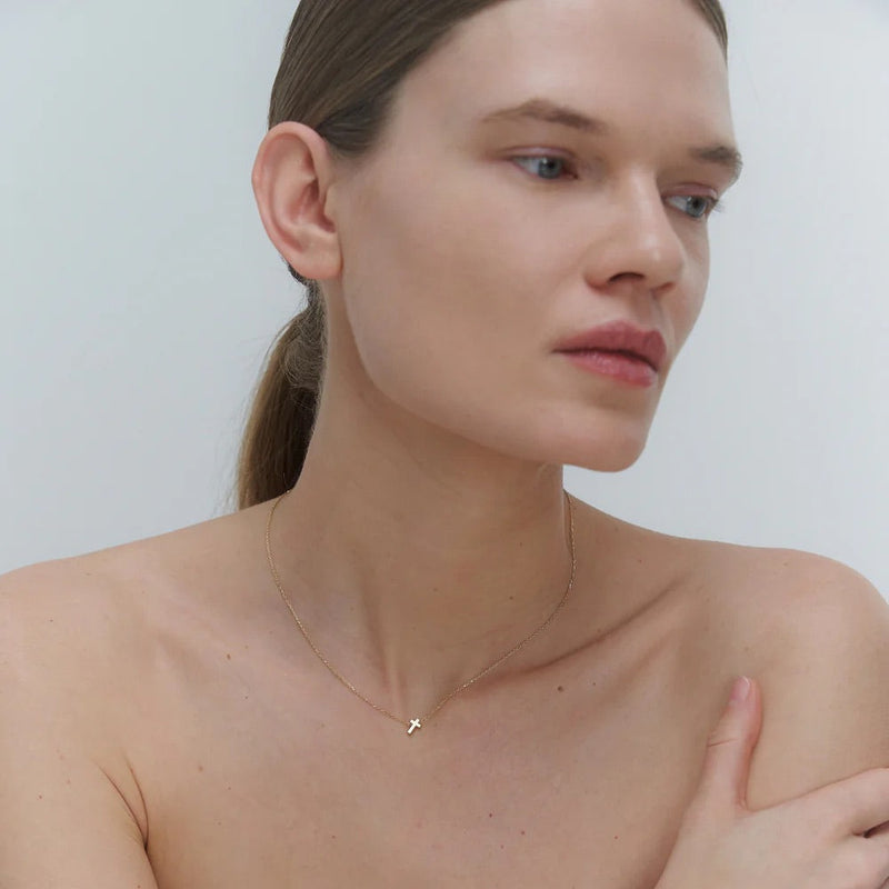 Woman wearing a delicate gold necklace with cross pendant against a plain background