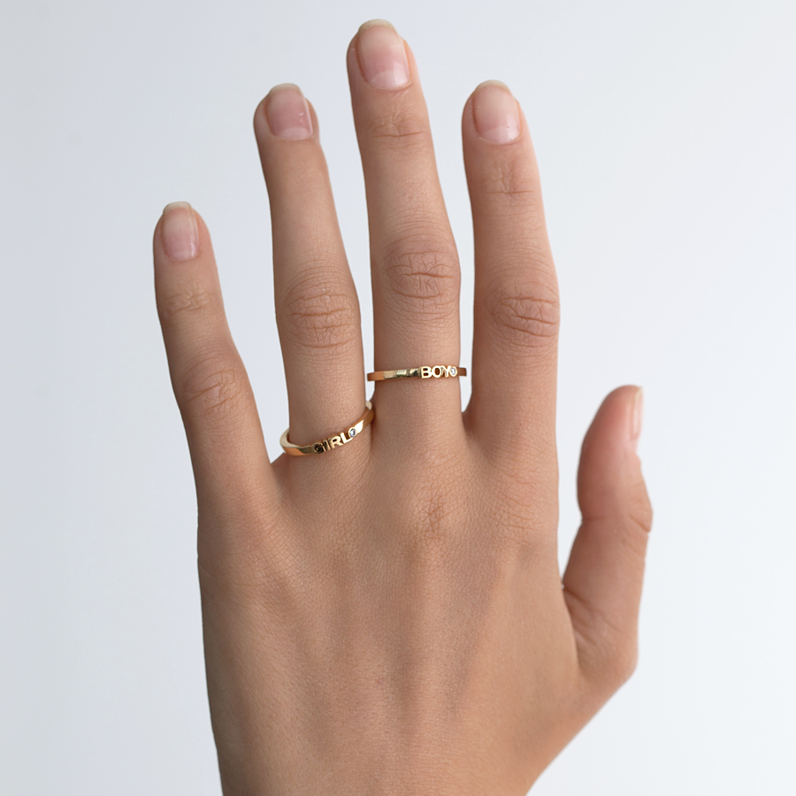 Hand wearing two gold and diamond rings titled "Boy" and "Girl".