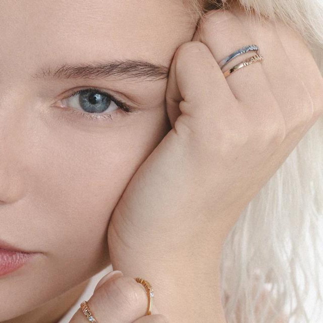 Woman wearing two gold rings with word Mama set with single diamond.