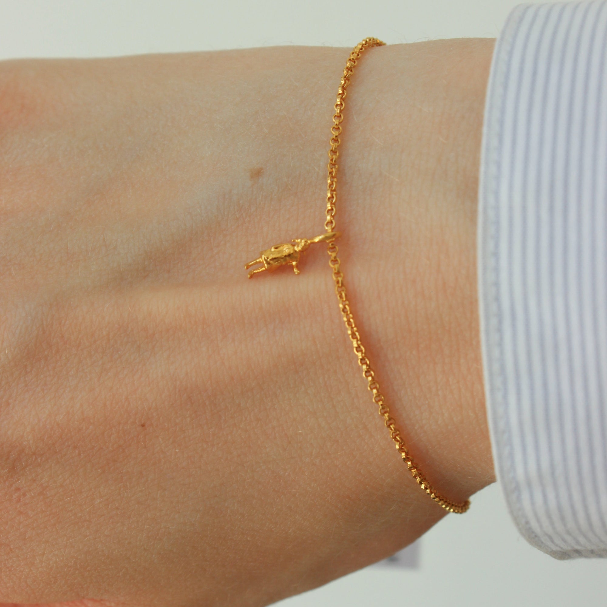 Gold-plated silver bracelet on a wrist with a plain background