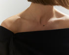 A close-up of a model's neck and upper chest wearing a delicate gold chain necklace with a small black faceted diamond, paired with a black off-the-shoulder top.