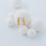 A pair of textured gold hoop earrings displayed on a large white foam ball, surrounded by smaller white foam balls against a light gray background.