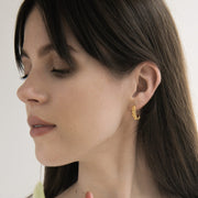 A close-up lifestyle shot of a woman with dark hair wearing a small gold crescent moon earring, against a clean white background.