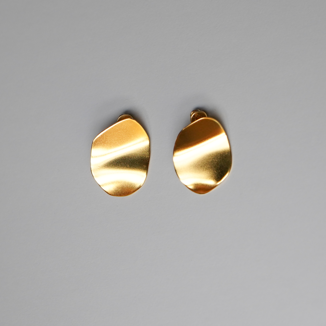 A pair of abstract, organic-shaped gold-plated silver earrings with a brushed metallic finish, displayed on a neutral gray background.