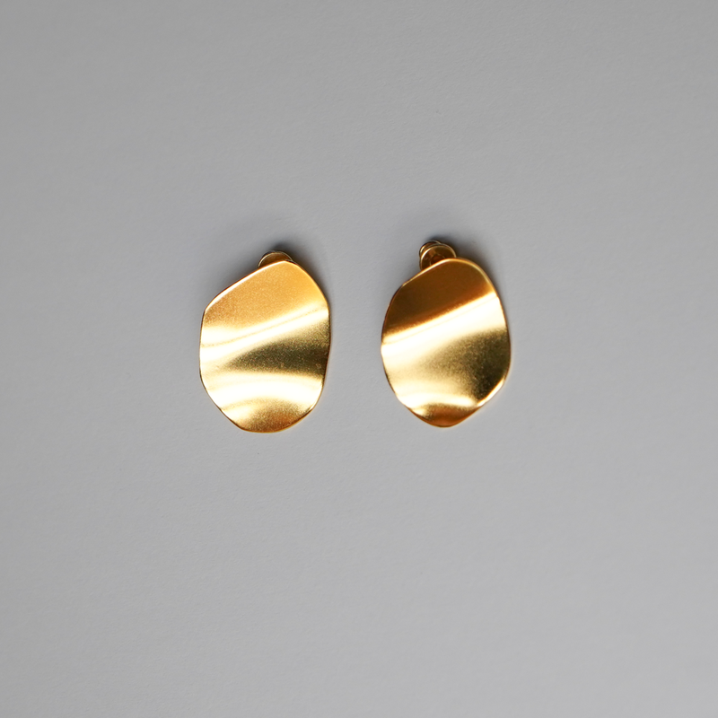 A pair of abstract, organic-shaped gold-plated silver earrings with a brushed metallic finish, displayed on a neutral gray background.
