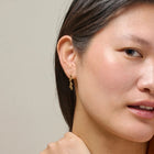 Close-up of a woman wearing gold earrings with a neutral background