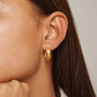 Close-up of a person wearing a gold hoop earring with a neutral background