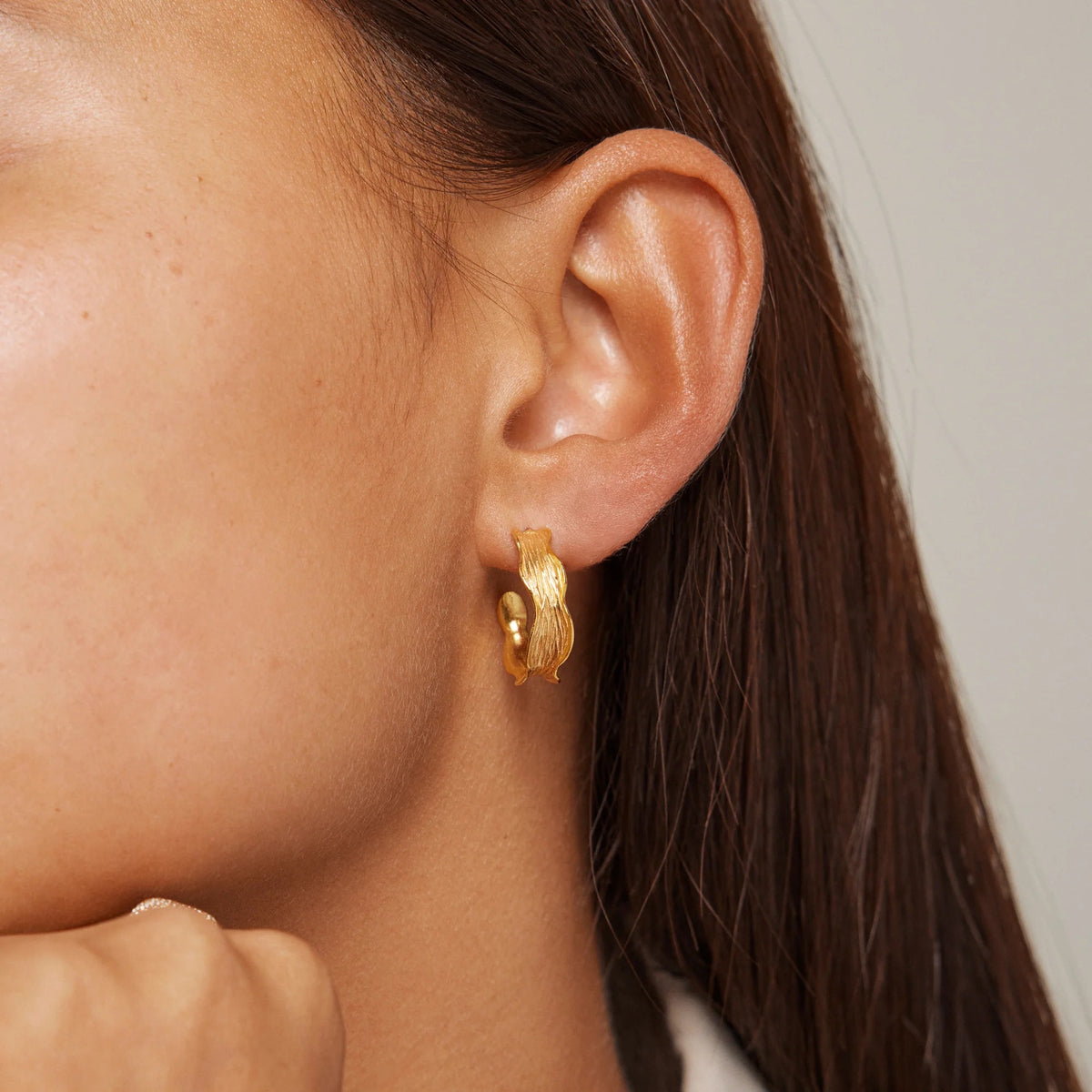 Close-up of a person wearing a gold hoop earring with a neutral background