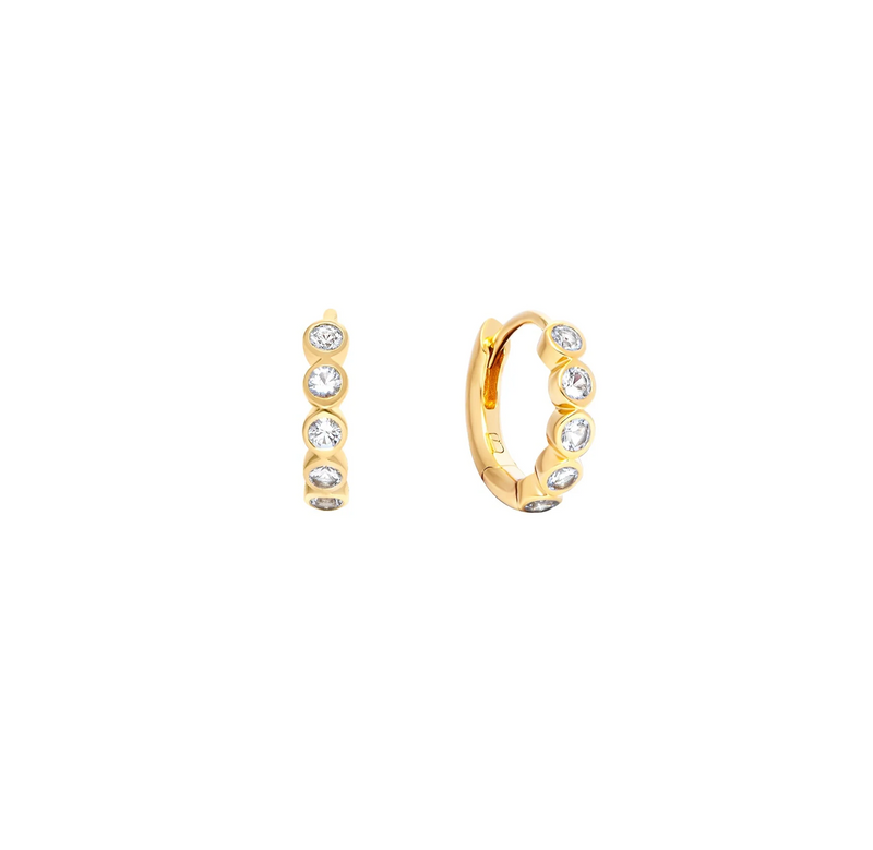 A pair of small gold-plated silver huggie hoop earrings, shown from the side and back, each adorned with five clear round-cut topaz gemstones in a bezel setting, on a solid white background.