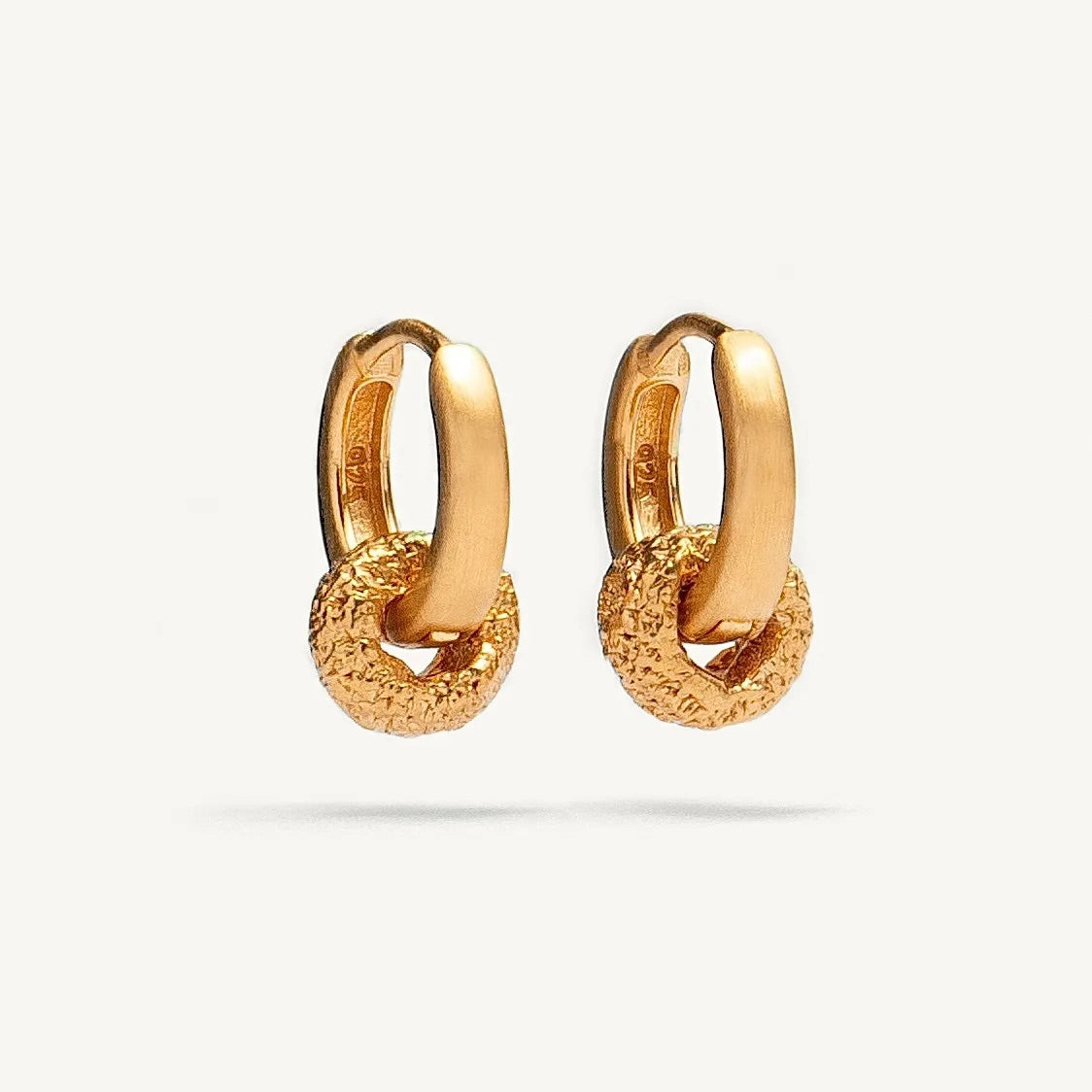 A pair of gold huggie hoop earrings with a textured, chain-link style lower section, shown on a clean off-white background.