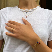 Person wearing a gold necklace with colorful beads and matching bracelet on a white shirt.