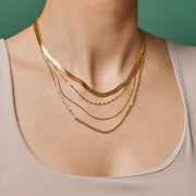 Three gold necklaces on a person's neck against a green background