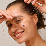Woman wearing a gold necklace with a blue pendant, smiling.