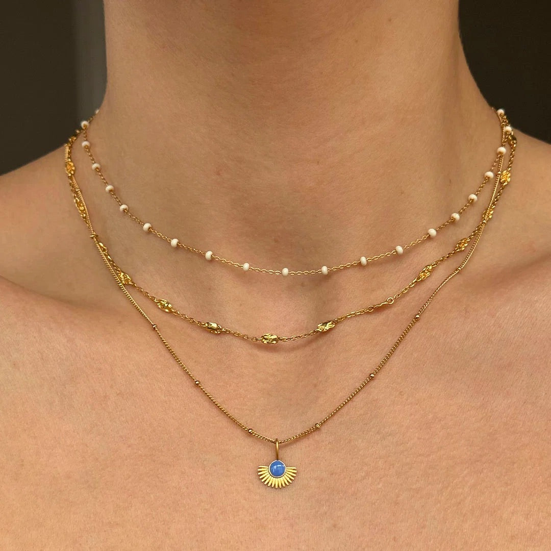 Two gold necklaces with a blue pendant on a person's neck against a dark background