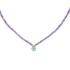 A delicate necklace featuring a strand of small purple amethyst beads and a central gold-tone pendant with a teardrop-shaped light blue gemstone, set against a plain white background.