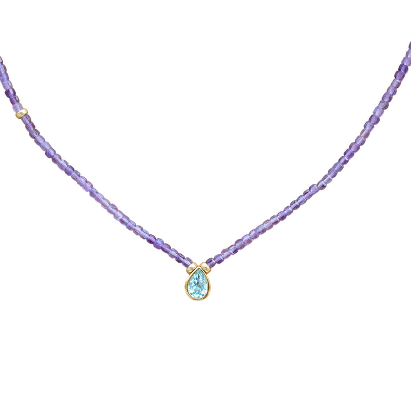 A delicate necklace featuring a strand of small purple amethyst beads and a central gold-tone pendant with a teardrop-shaped light blue gemstone, set against a plain white background.