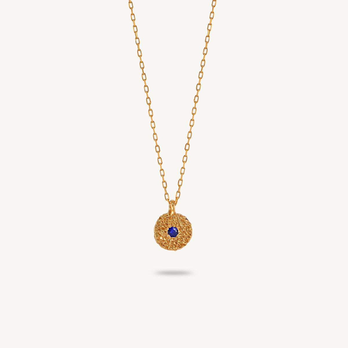 Gold-plated silver chain necklace featuring a round, textured disc pendant with a small blue sapphire set in the center.