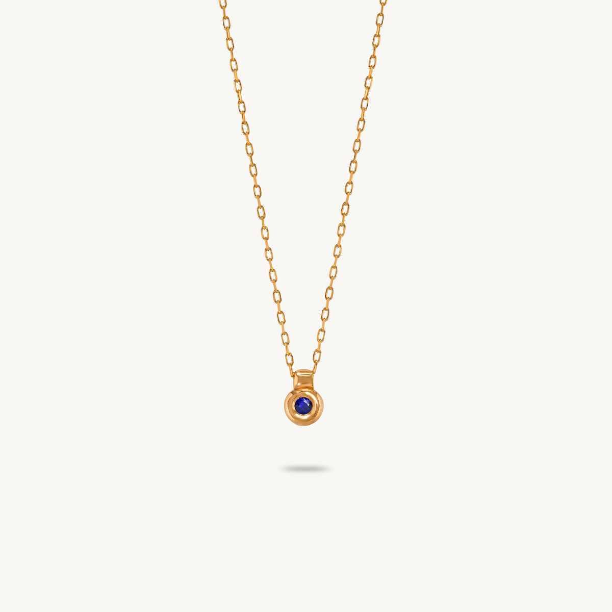 A gold-plated silver pendant featuring a smooth, sculptural bezel framing a single central blue sapphire.