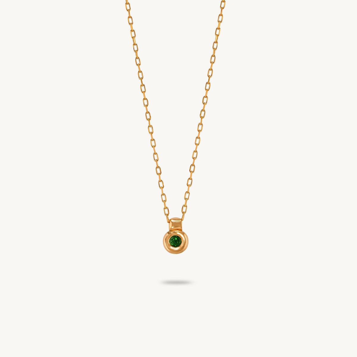 A gold-plated silver pendant featuring a smooth, sculptural bezel framing a single central emerald.