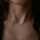 A delicate gold-plated silver chain necklace with a single small white pearl pendant, shown worn on a person's neck and upper chest.