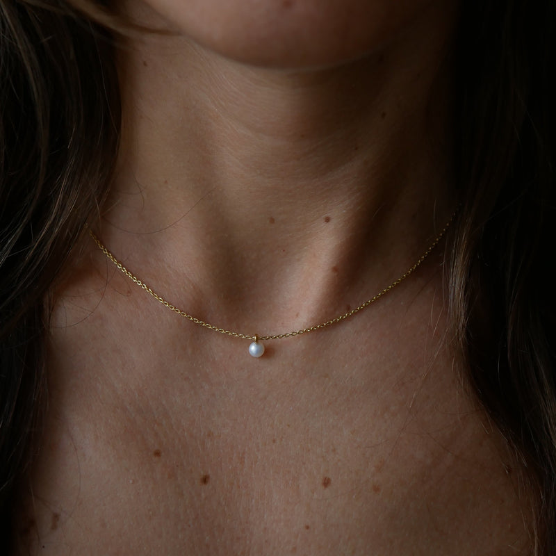 A delicate gold-plated silver chain necklace with a single small white pearl pendant, shown worn on a person's neck and upper chest.