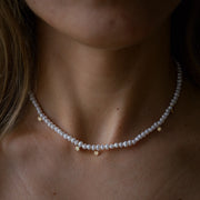 A close-up of a model's neck and collarbone wearing a delicate white pearl necklace with small gold-plated silver accents.