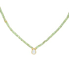 A delicate necklace featuring a strand of small, faceted peridot beads with a gold-tone setting holding a teardrop-shaped zirconium, shown against a plain white background.