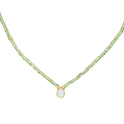A delicate necklace featuring a strand of small, faceted peridot beads with a gold-tone setting holding a teardrop-shaped zirconium, shown against a plain white background.