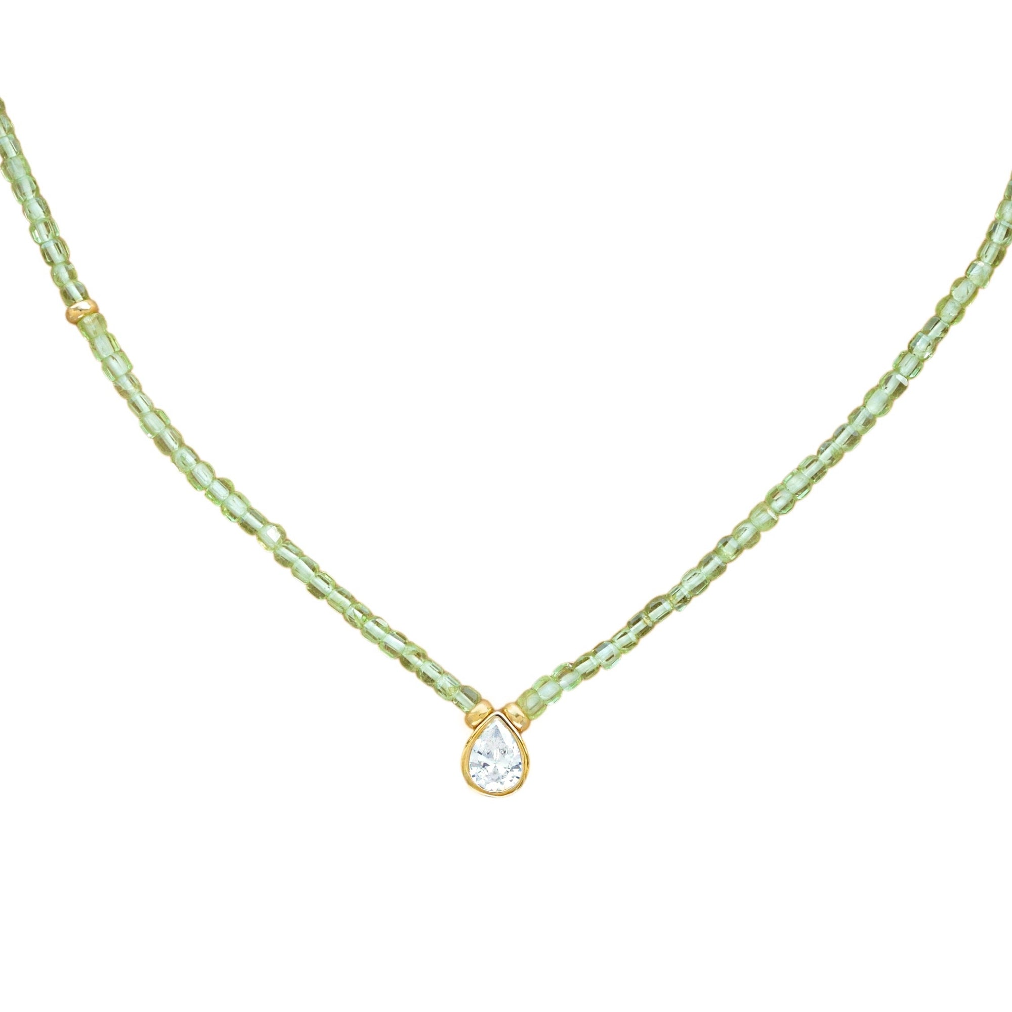 A delicate necklace featuring a strand of small, faceted peridot beads with a gold-tone setting holding a teardrop-shaped zirconium, shown against a plain white background.