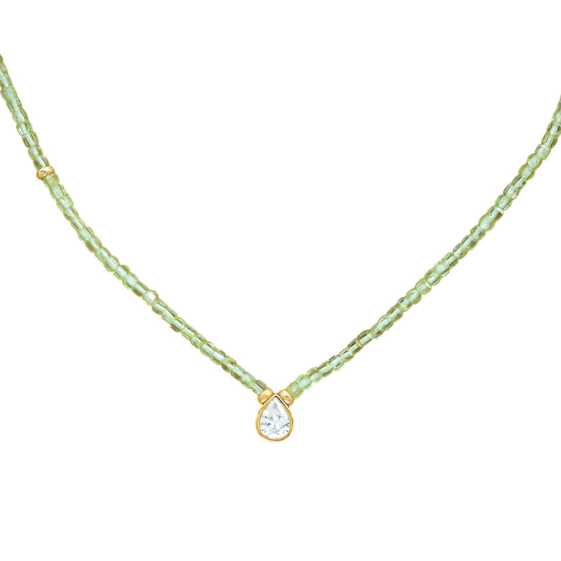 A delicate necklace featuring a strand of small, faceted peridot beads with a gold-tone setting holding a teardrop-shaped zirconium, shown against a plain white background.
