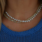 A close-up of a person's neck and upper chest wearing a pearl necklace paired with pale green prehnite beads necklace.