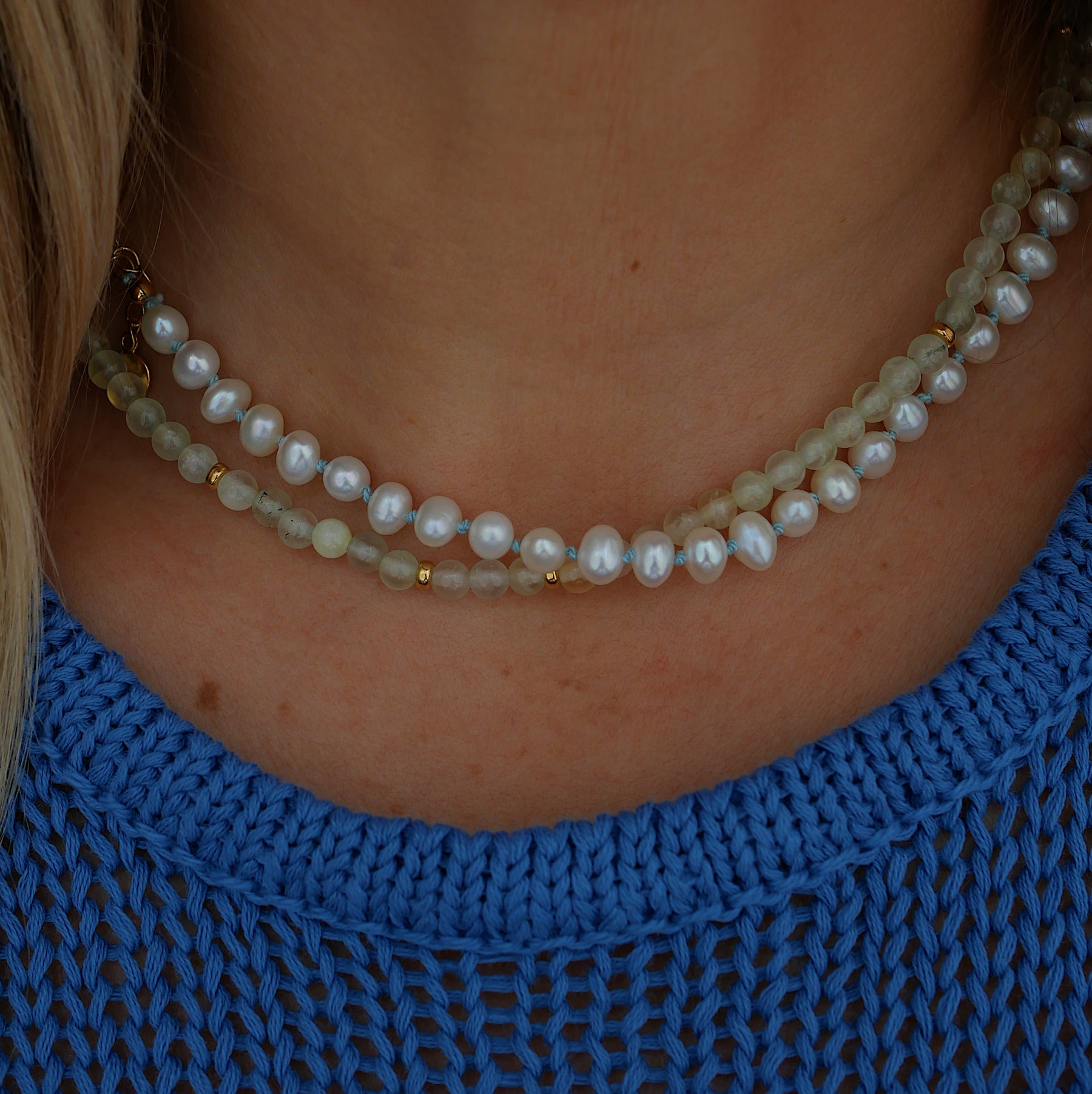 A close-up of a person's neck and upper chest wearing a pearl necklace paired with pale green prehnite beads necklace.