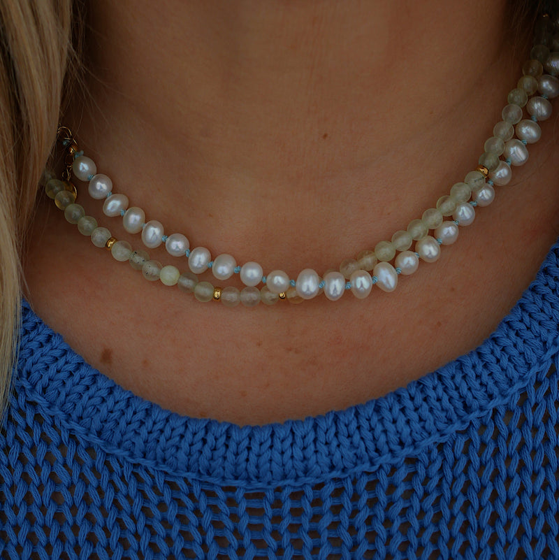 A close-up of a person's neck and upper chest wearing a pearl necklace paired with pale green prehnite beads necklace.