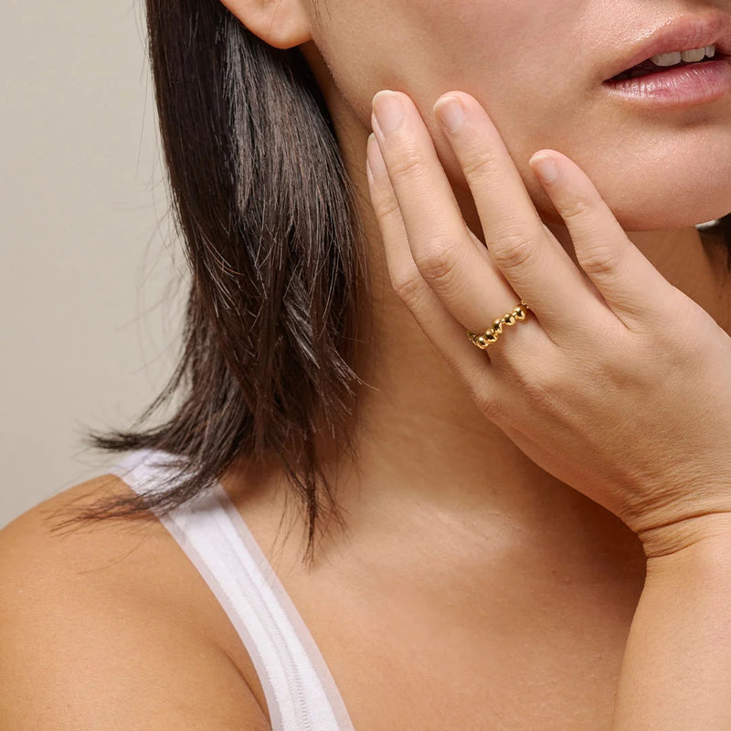 Woman wearing a gold-plated silver ring on her finger, with a neutral background