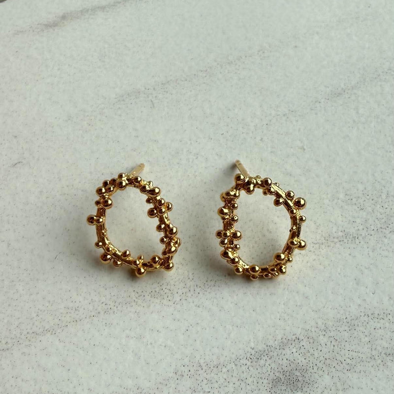 A pair of gold hoop earrings with a textured, beaded circular design, displayed on a light gray marble surface.