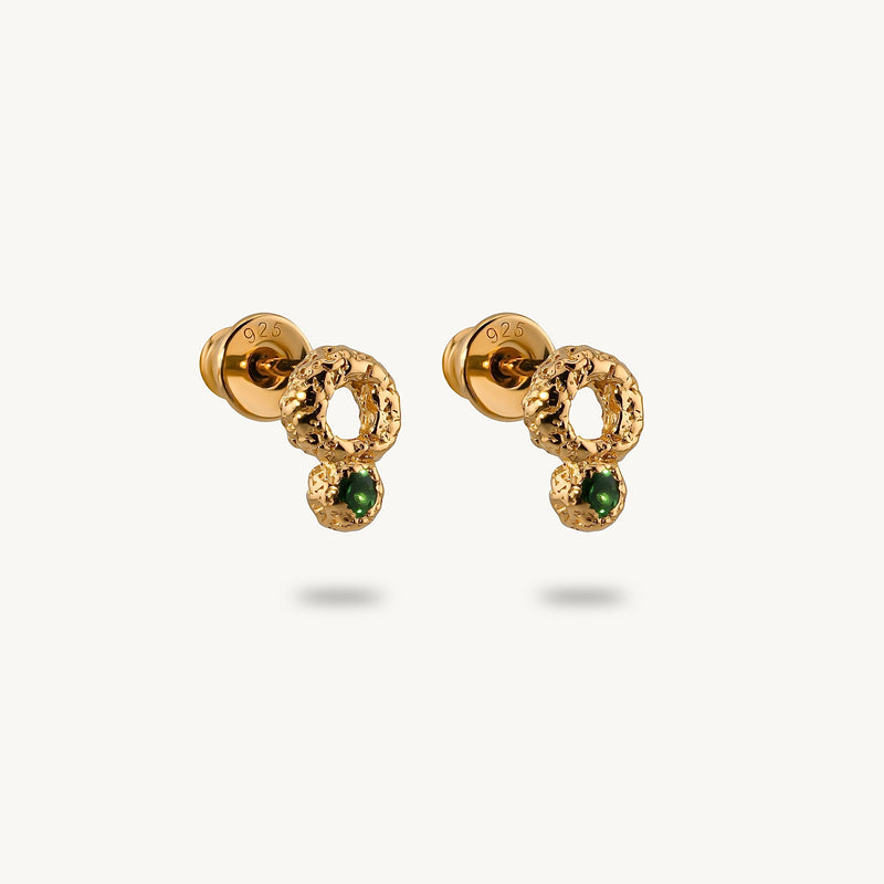 A pair of stud earrings made from gold-plated silver, featuring a raw, artisanal textured surface and vibrant green emeralds.
