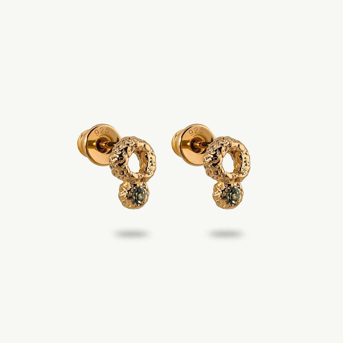 A pair of gold dangle earrings with textured circular loops, small clear pavé accents, and a central round green sapphire, shown on a light cream background.