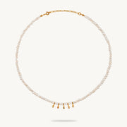 A delicate pearl necklace with a gold chain extender and five small gold teardrop charms at the center, displayed on a clean off-white background.