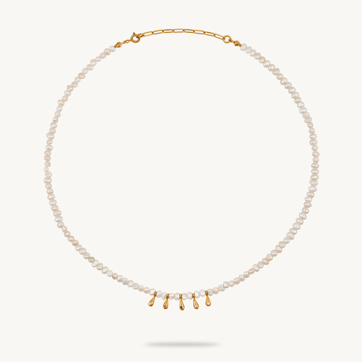 A delicate pearl necklace with a gold chain extender and five small gold teardrop charms at the center, displayed on a clean off-white background.