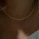 A delicate pearl necklace worn on a person's neck, shown in a close-up shot with warm, dim lighting.
