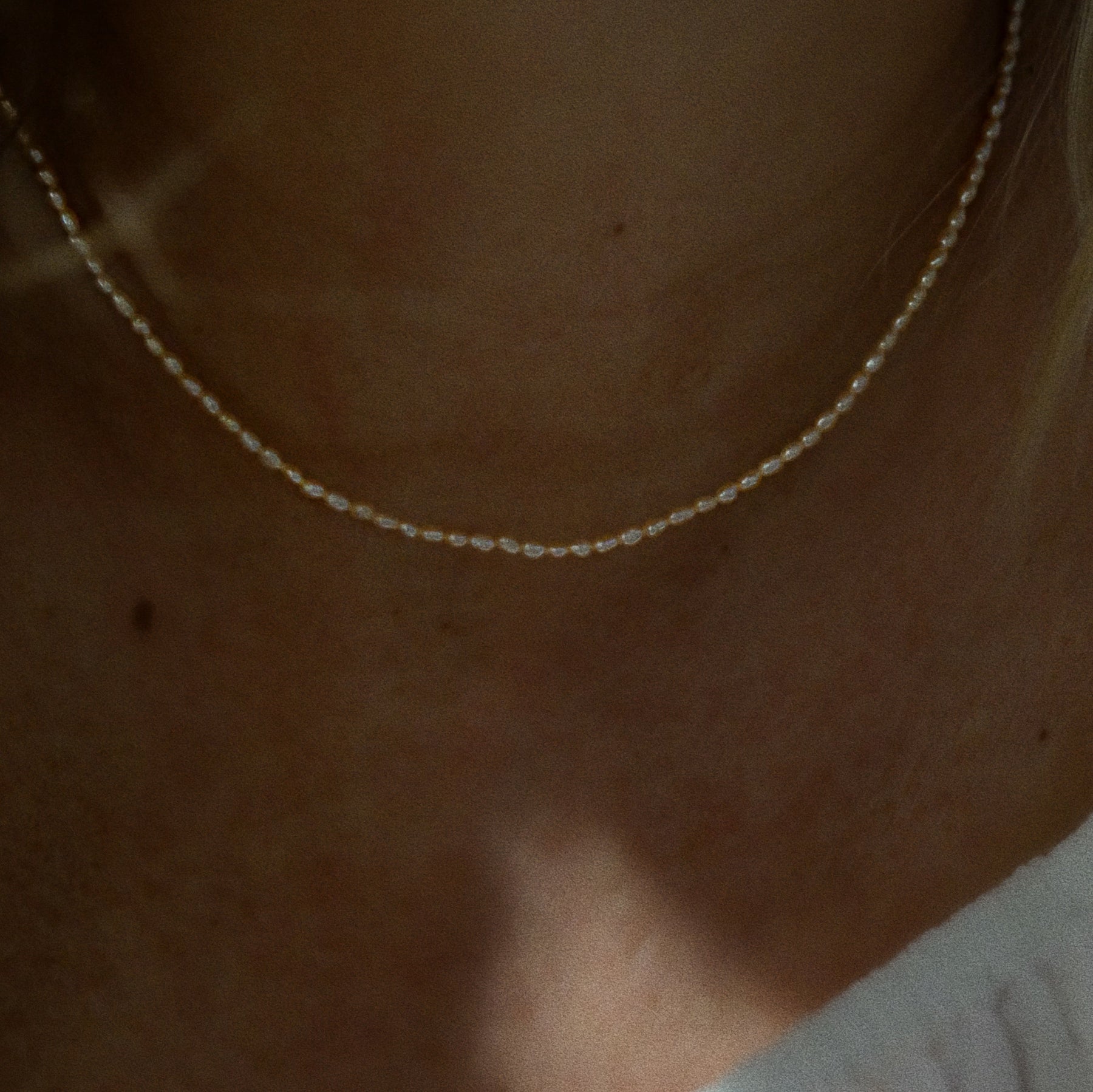 A delicate pearl necklace worn on a person's neck, shown in a close-up shot with warm, dim lighting.