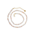 A beaded necklace featuring white and pale pink baroque pearls threaded with small gold-toned beads, finished with a gold lobster clasp, extender chain, and round brand tag.