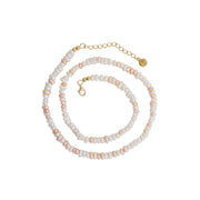 A beaded necklace featuring white and pale pink baroque pearls threaded with small gold-toned beads, finished with a gold lobster clasp, extender chain, and round brand tag.