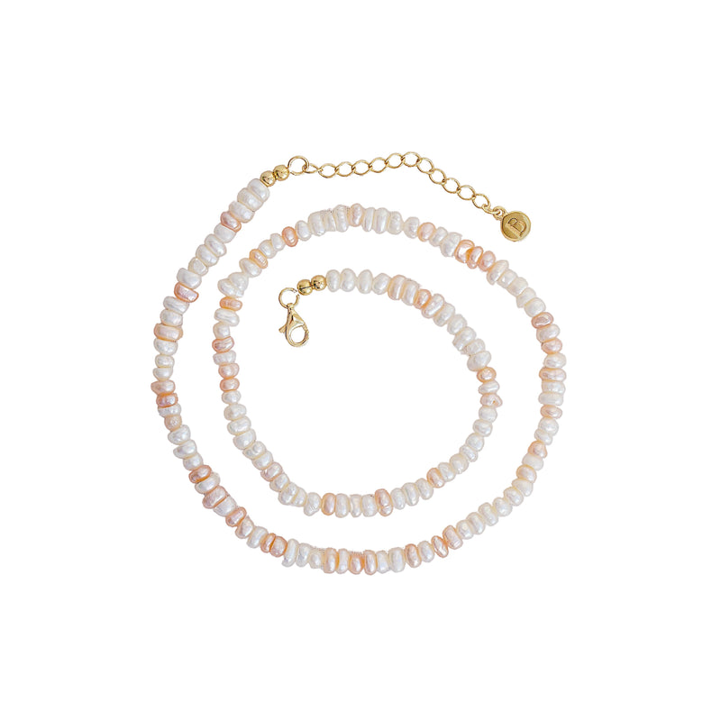 A beaded necklace featuring white and pale pink baroque pearls threaded with small gold-toned beads, finished with a gold lobster clasp, extender chain, and round brand tag.
