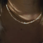 A close-up of a person wearing a delicate pearl choker necklace, with warm, moody lighting highlighting the lustrous beads against the skin.