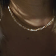 A close-up of a person wearing a delicate pearl choker necklace, with warm, moody lighting highlighting the lustrous beads against the skin.