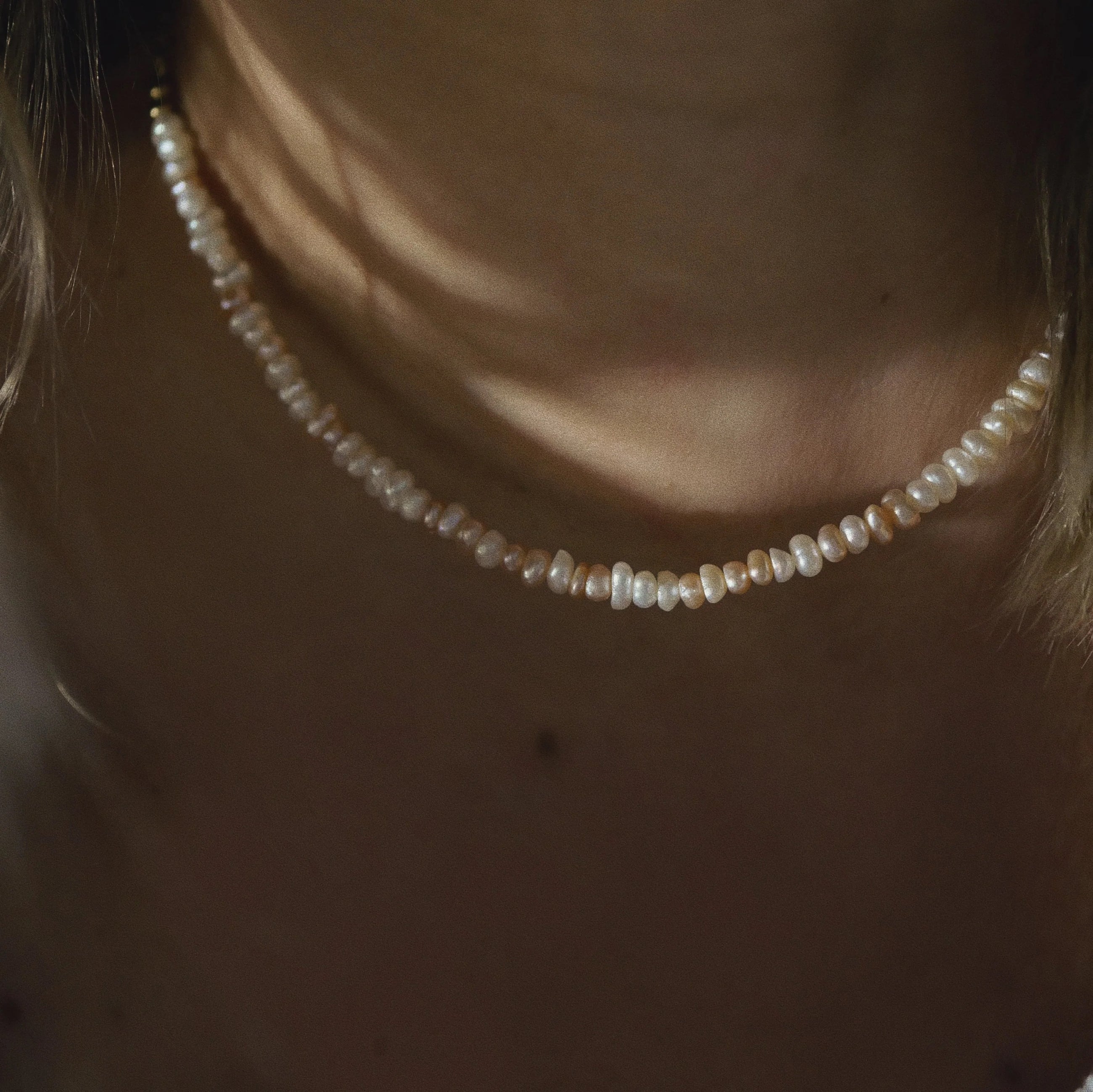 A close-up of a person wearing a delicate pearl choker necklace, with warm, moody lighting highlighting the lustrous beads against the skin.
