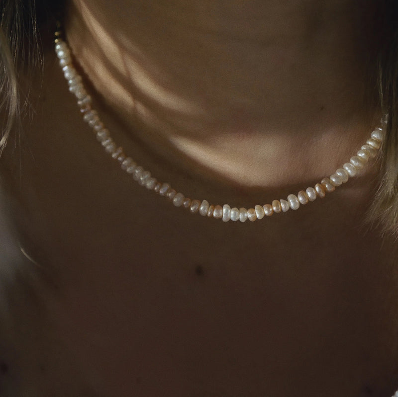 A close-up of a person wearing a delicate pearl choker necklace, with warm, moody lighting highlighting the lustrous beads against the skin.